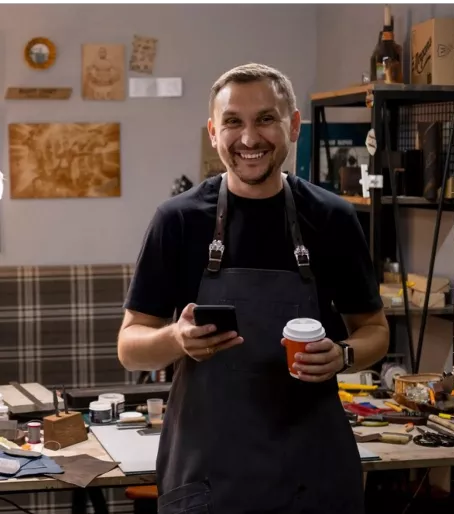 Comerciante sorrindo e gerenciando seu negócio pelo celular